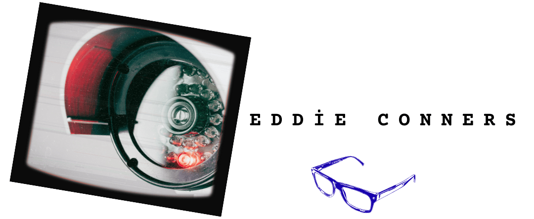 Close-up of a security camera inside an old TV screen. The text says Eddie Conners. Below it is a pair of blue glasses.