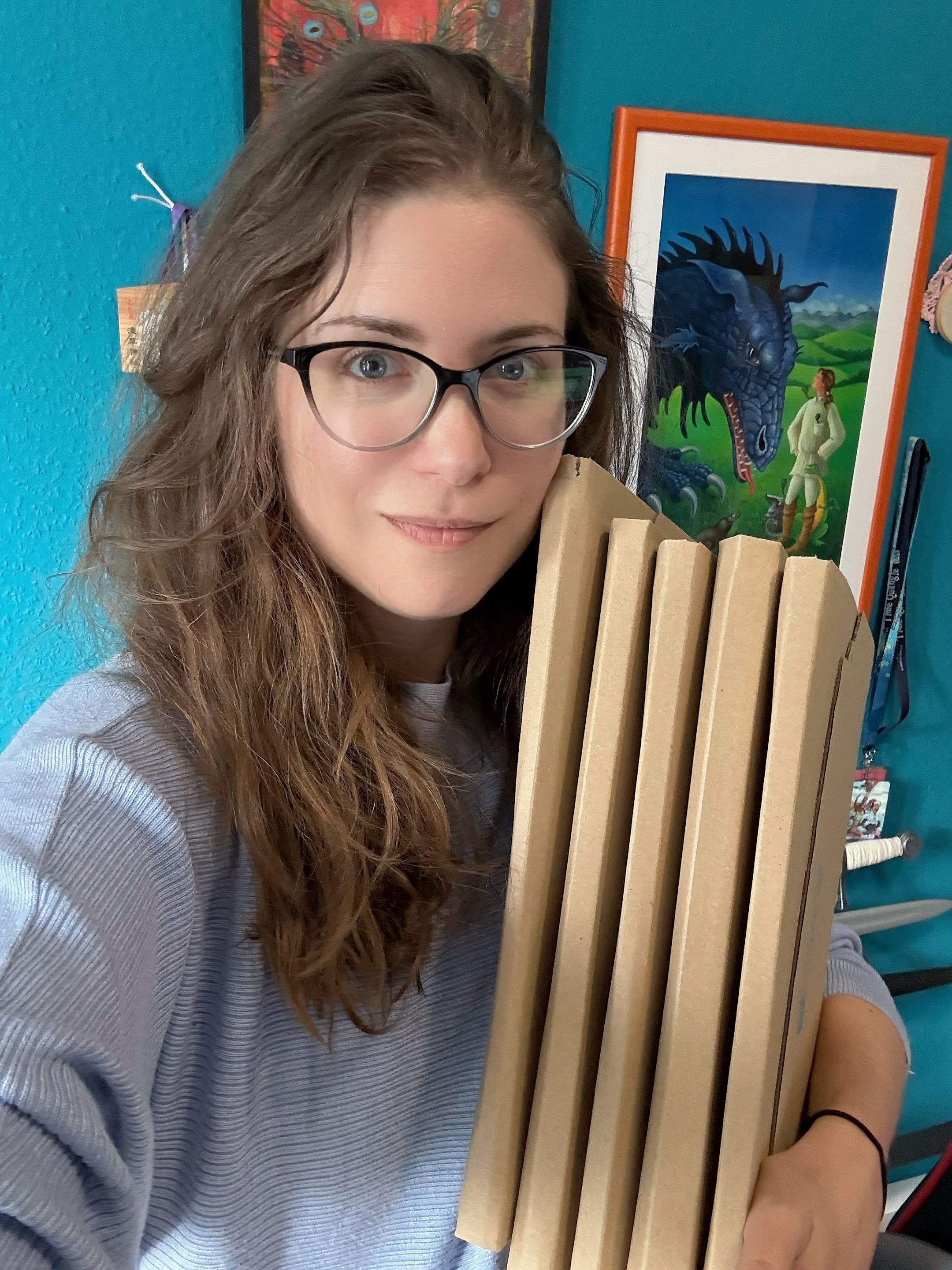 A blonde woman in a light blue top and glasses smiling at the camera. She is holding five packages in her arms.