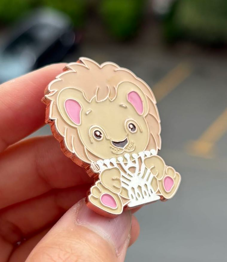Hand holding an enamel pin of a lion holding a silver menorah.