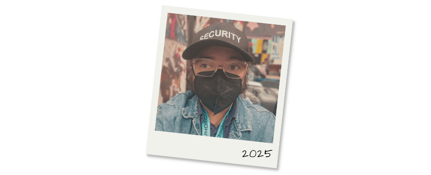 Polaroid mockup featuring a selfie of yours truly: a brown person with short hair and glasses, wearing a denim jacket, a black face mask, and a black hat that says security.