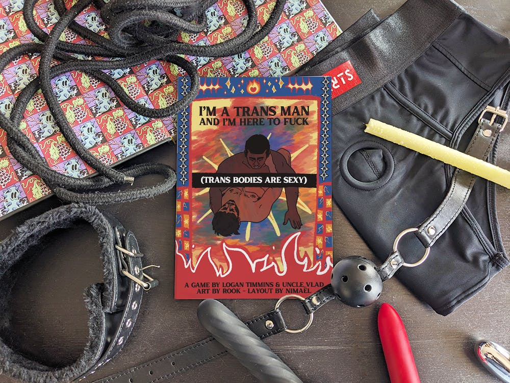 Mockup of the A5 booklet I'm a trans man and I'm here to fuck (trans bodies are sexy) by Logan, Uncle Vlad, Rook and Nimaël. The booklet is surrounded by sex toys and accessories (cord, gag, collar, candle...) and an open book to add some pretty colors (the book is Boy Island by Leo Fox).