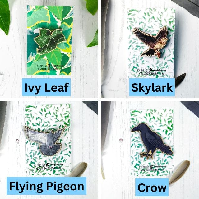 a grid of four wooden pins created from illustrations by Loadofolbobbins. Clockwise from top left a dark green ivy leaf, a flying skylark, a crow and a flying pigeon. https://www.backerkit.com/c/projects/loadofolbobbins/loadofolbobbins-holiday-shop