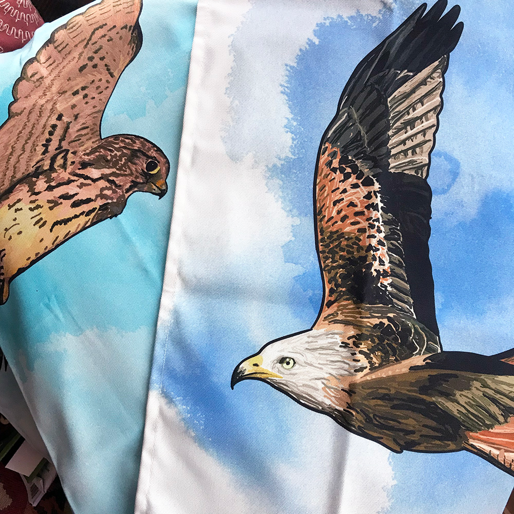 a close up of two tea towels. The one on the left shows a glimpse of a female kestrel hovering. The one on the right shows a red kite flying against an inky blue wash background.
